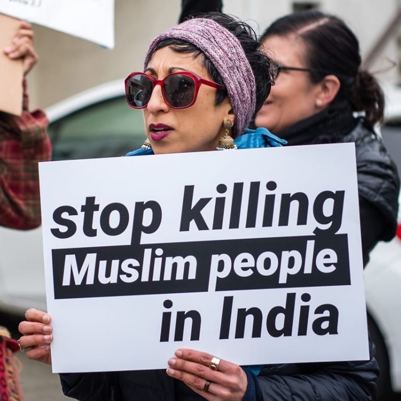 South Asian woman in red sun glasses holding a sign that reads stop killing muslim people in India